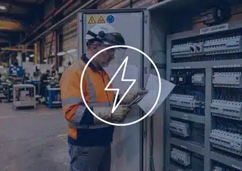 Électricien habilité BR consultant le schéma de protection d'un tableau BT 230V/400V — EPI complet : visière de protection faciale, casque, gants isolants